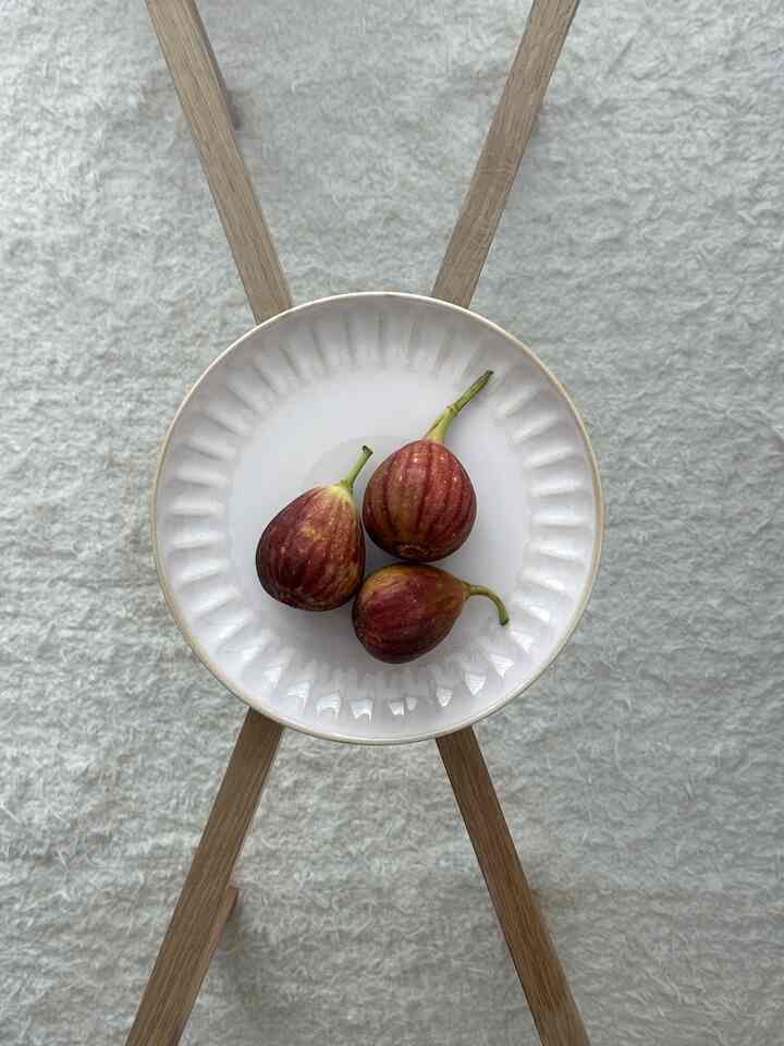 ナチュラルな木製脚のサイドテーブルの上に白い皿と赤いイチジクが置かれた明るい色調の空間