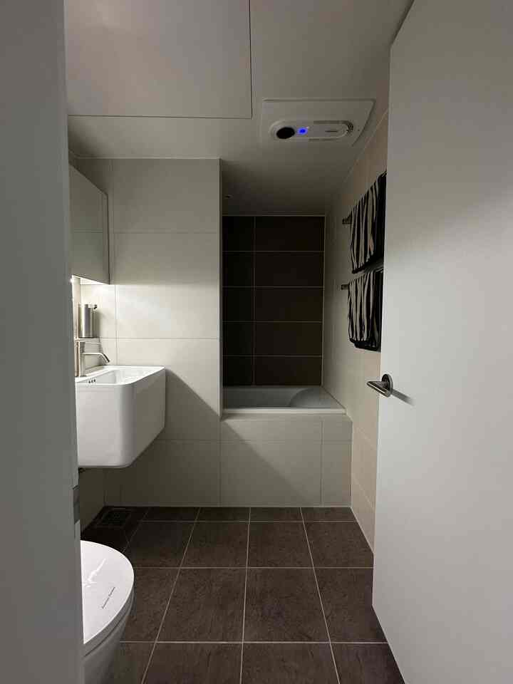 ホワイトとブラウンのツートンのトイレ、洗面台とバスタブが配置された清潔感のあるバスルーム