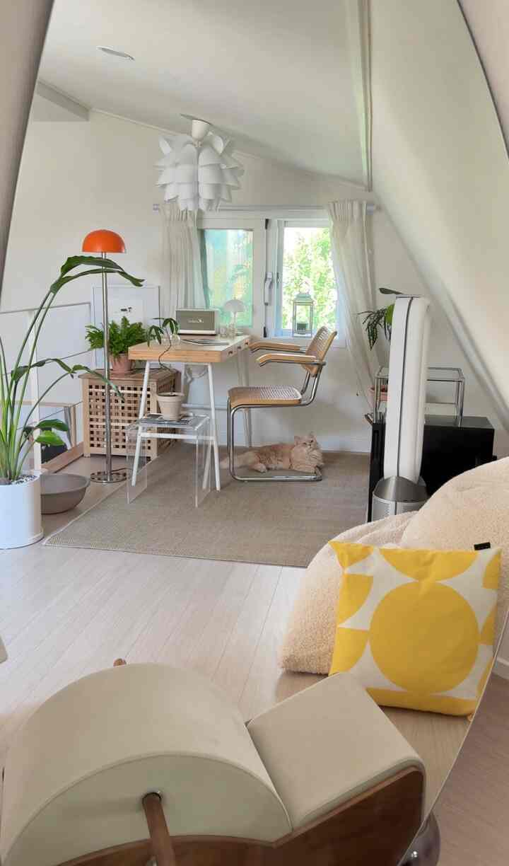 白とベージュのナチュラルモダンなリビング兼ホームオフィス空間、窓際の机と椅子、カーペットの上に横たわる猫が配置された印象的な空間