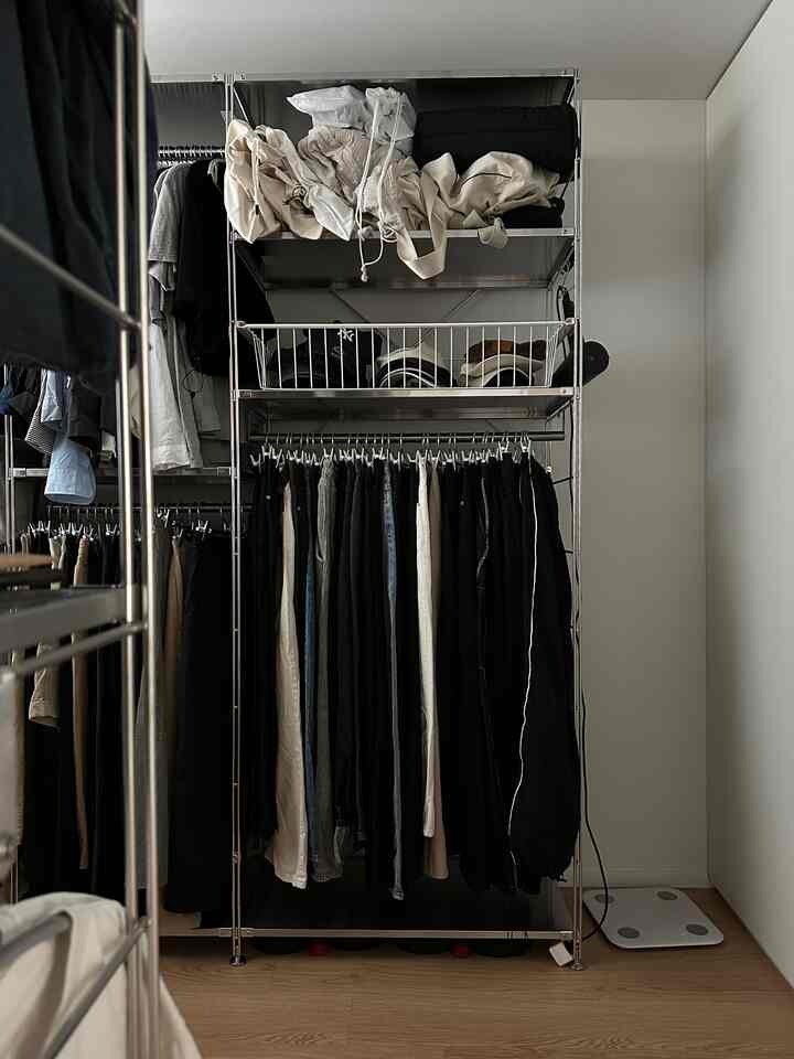 白い壁と茶色い木の床が調和するナチュラルなウォークインクローゼット、金属製収納棚と整理された衣服が配置された印象的な空間