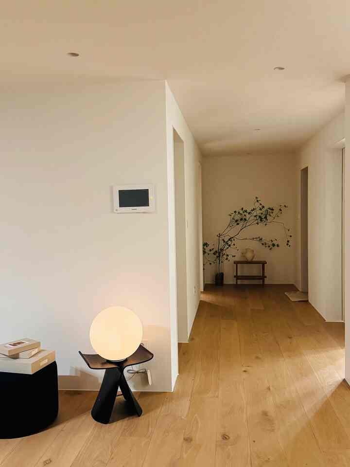 白い壁と明るい木目調の床のリビング兼廊下の空間、シンプルなスツールと丸い照明が配置されたナチュラルなインテリア