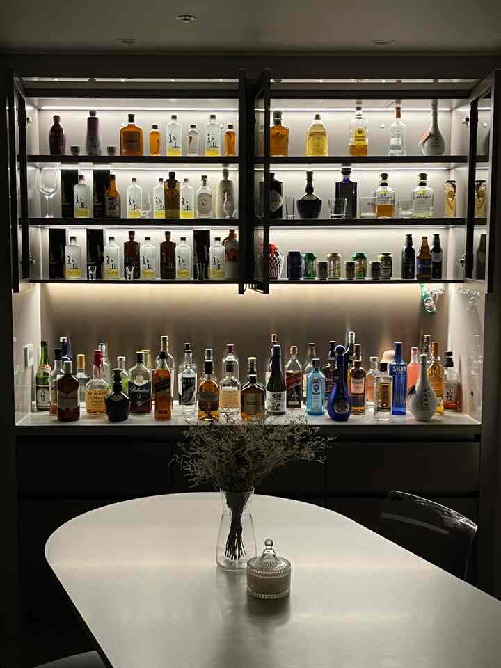 落ち着いた照明が灯るモダンなダイニング、ホームバーと透明な椅子がある白いダイニングテーブルの空間