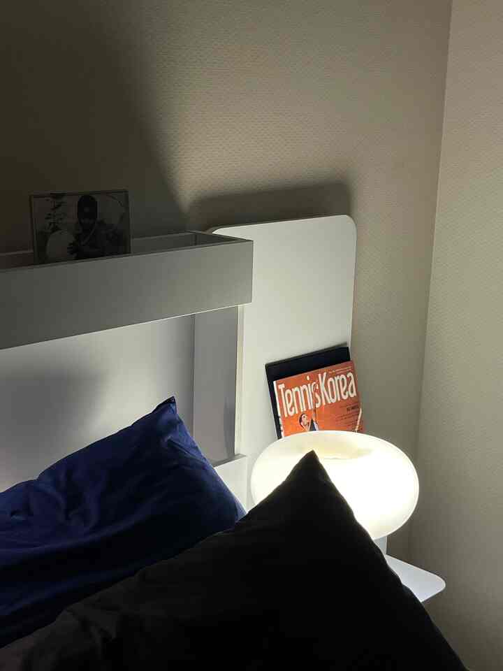 白とネイビーの調和がある寝室、柔らかなムードライトとミッドセンチュリーモダンのベッドが配置された雰囲気のあるインテリア