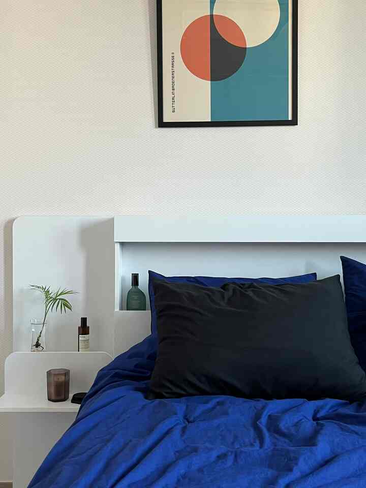 トーンダウンしたブルーとブラックの枕が置かれた白のミッドセンチュリーモダンスタイル寝室、幾何学模様の額縁アートが壁に掛けられた落ち着いた空間