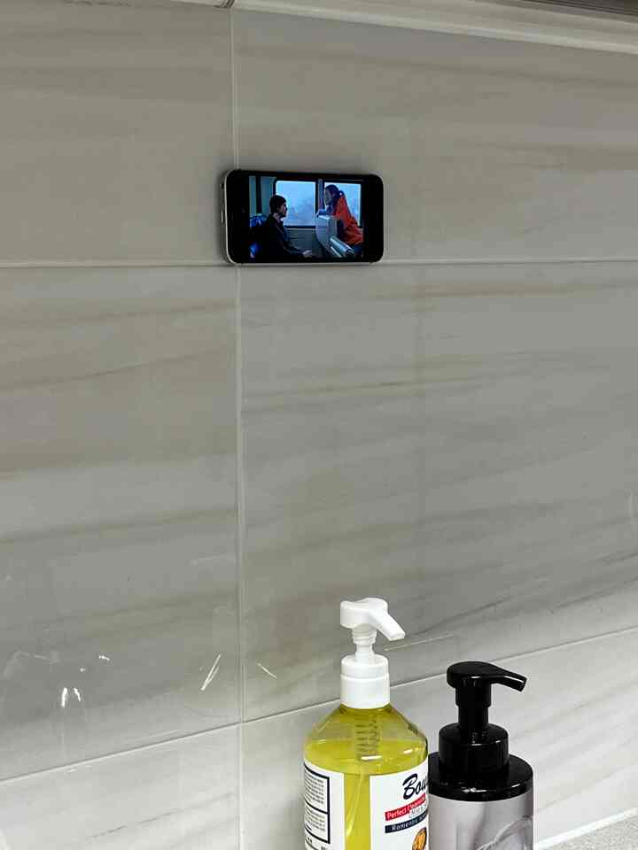 白いタイルの壁が特徴的なキッチン、下部に黄色と黒の洗剤ボトルが置かれ、壁にスマートフォンが貼り付けられて動画を再生している清潔な空間