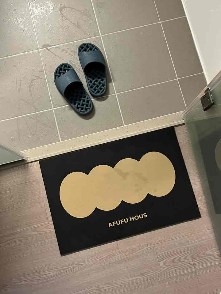 グレーのタイル床と黒のバスマット、ネイビーブルーのバススリッパが配置されたバスルーム入口の雰囲気ある空間