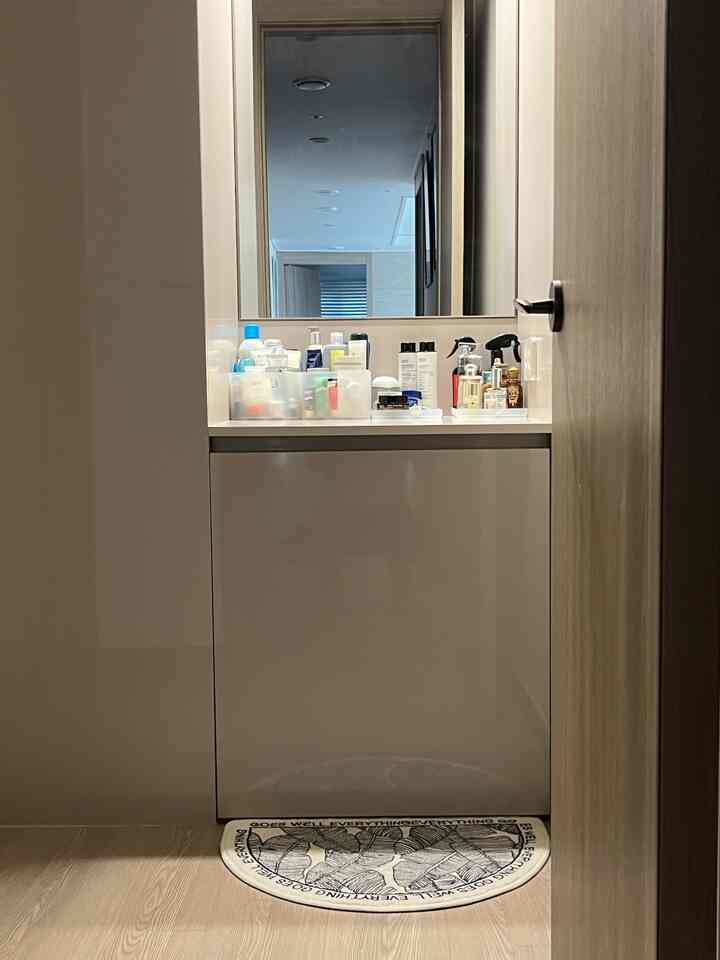 ナチュラルカラーと木目調の調和があるお手洗い、洗面台の上に様々な化粧品が整然と置かれた印象的な空間