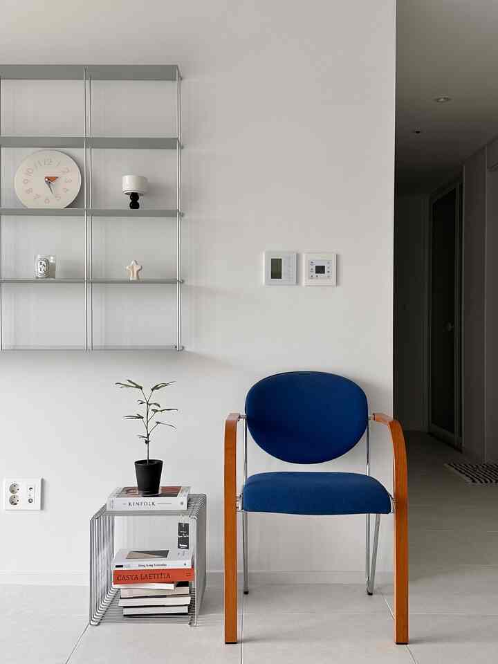 白い壁と床に置かれた深い青色のヴィンテージ風アームチェアと左側の金属製棚があるシンプルなリビングスペース