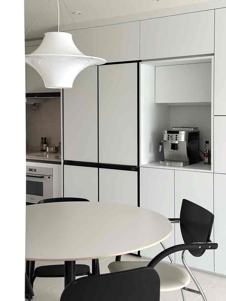 白と黒のトーンのキッチンスペース、円形のダイニングテーブルとコーヒーマシンが配置された清潔でモダンなインテリア