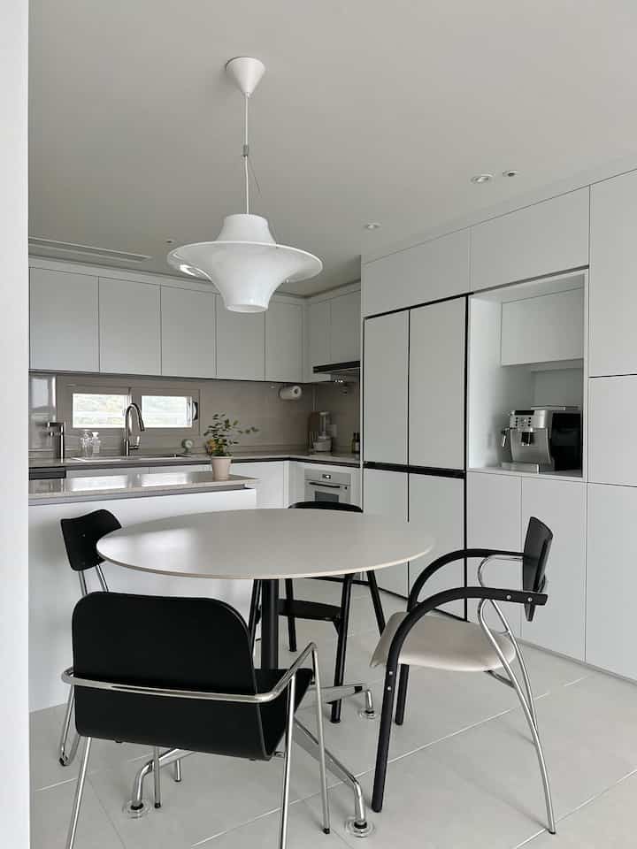 ホワイトとブラックのトーンが印象的なモダンなキッチンとダイニングルーム、丸テーブルと異なるデザインの椅子が配置されたシンプルな空間