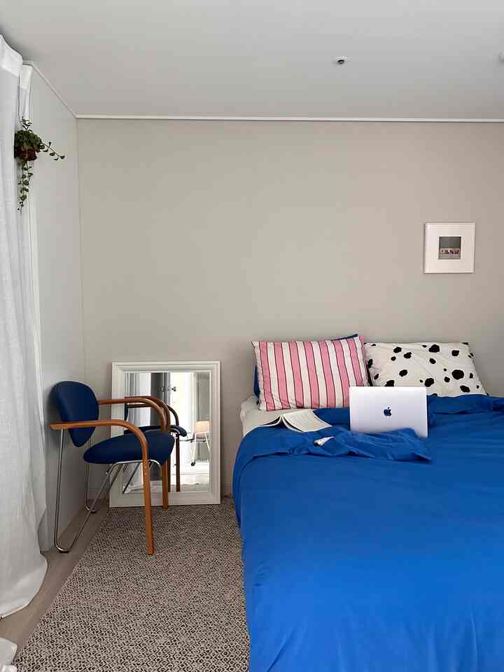 ナチュラルカラーの寝室、青い寝具とヴィンテージのアームチェア、鏡が配置された雰囲気のあるインテリア