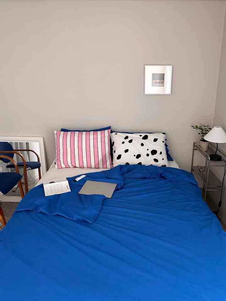 青と白のトーンが特徴の寝室、シンプルなベッドと枕、ナイトテーブルと本が配置された落ち着いた雰囲気のインテリア