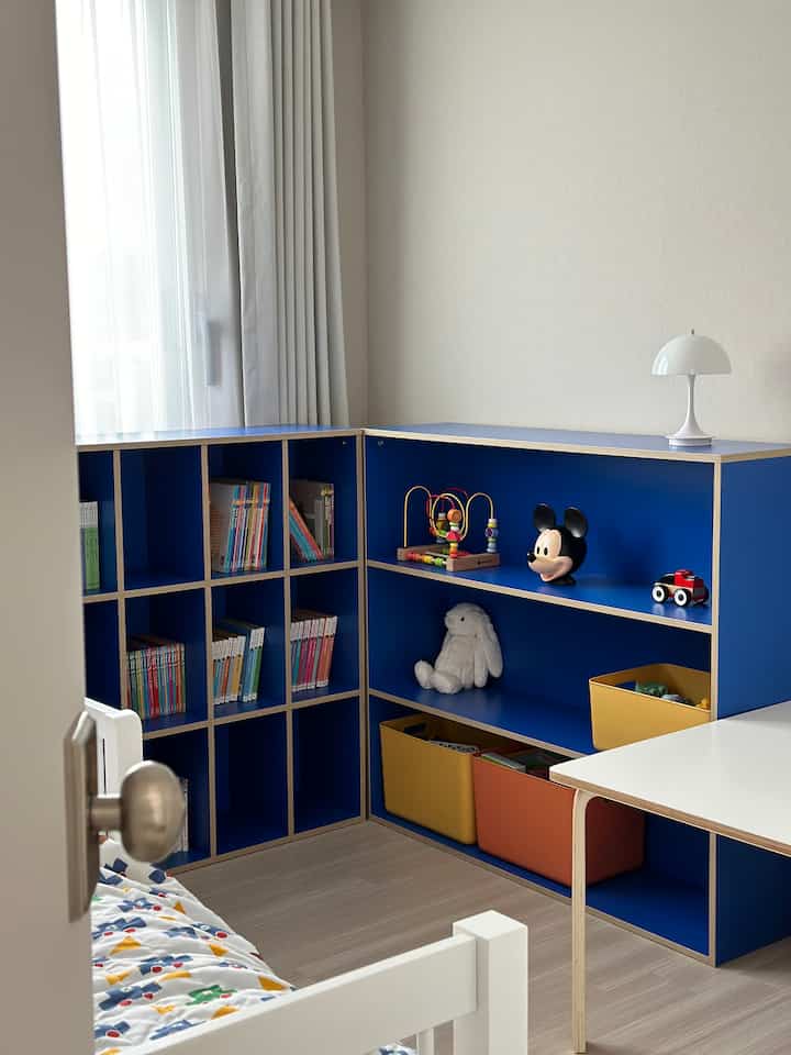 白と青のトーンの子供部屋、書棚とデスク、玩具収納が配置された印象的な空間
