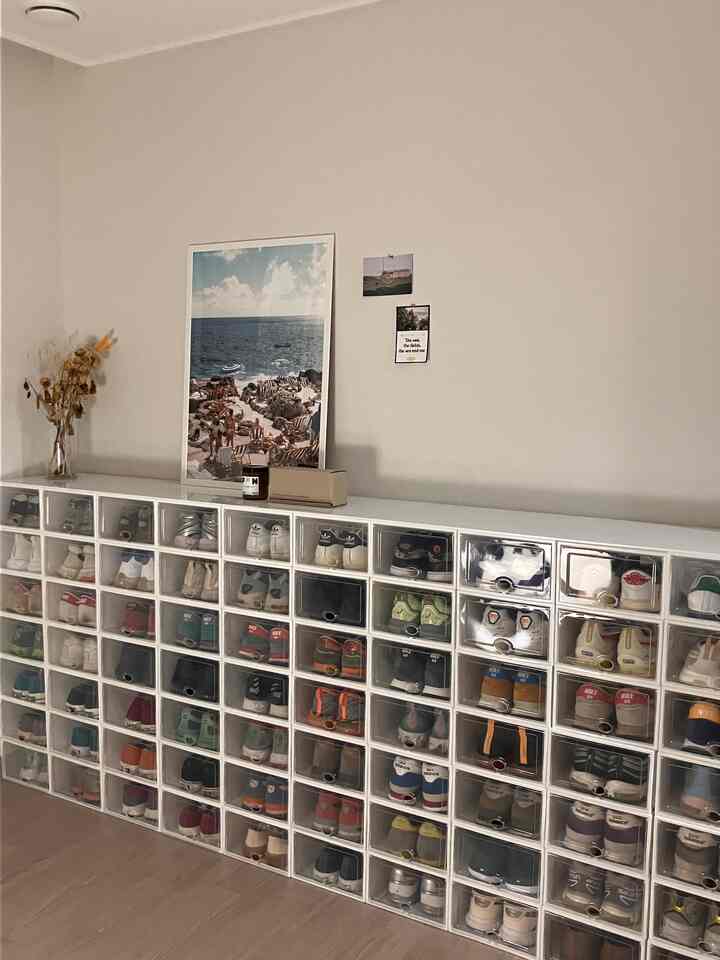 ベージュの床と白いシューズラックがあるミニマルな玄関空間、海のポスターとドライフラワーの飾り付き