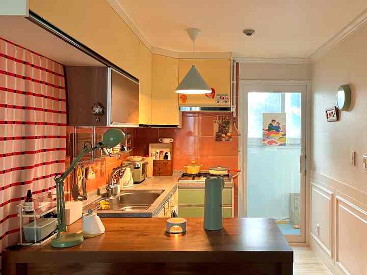 温かみのあるベージュと木目調のナチュラルなキッチン、黄色いキャビネットとペンダントライトが印象的なコンパクトな空間