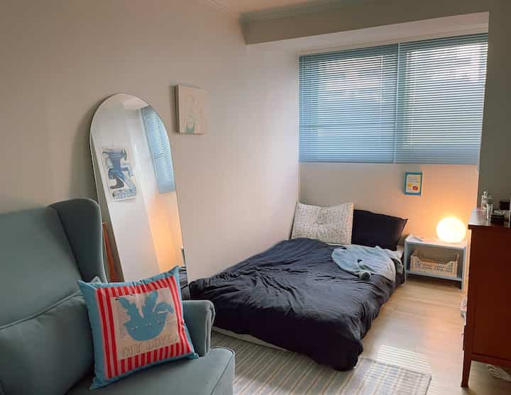 ブルーとブラウンのトーンの寝室、シンプルなベッドとブラインド、快適なアームチェアが配置されたモダンでナチュラルな雰囲気のインテリア