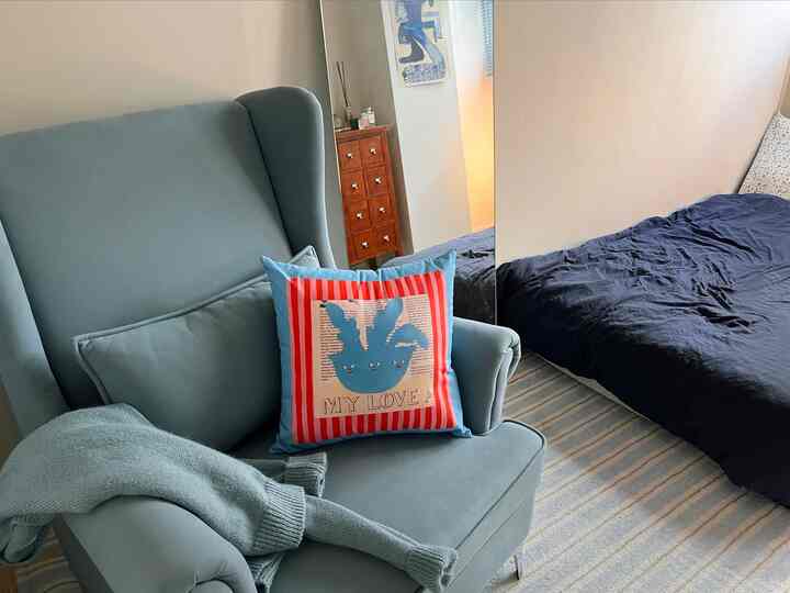 パステルトーンのブルーの寝室、1人掛けのアームチェアとネイビーの寝具が配置された雰囲気のある空間