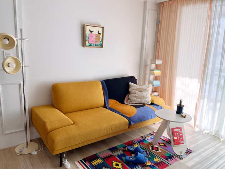 温かみのあるマスタード色のソファとピンクのストライプカーテンが配置された明るいリビングスペース