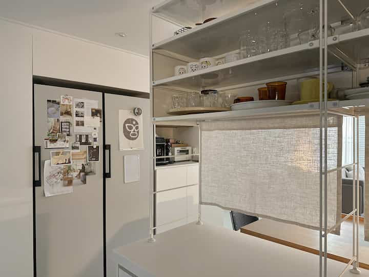 清潔感のあるホワイト調のキッチン、オープンシェルフとカーテンが配置され、居心地良く実用的な雰囲気を演出している