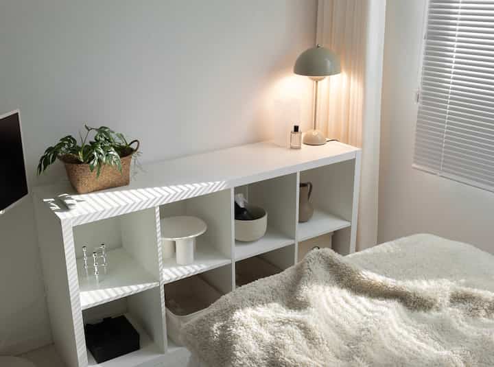 白を基調としたゲストルーム、イケアのKALLAXシェルフと暖かい照明が配置された心地よい収納空間
