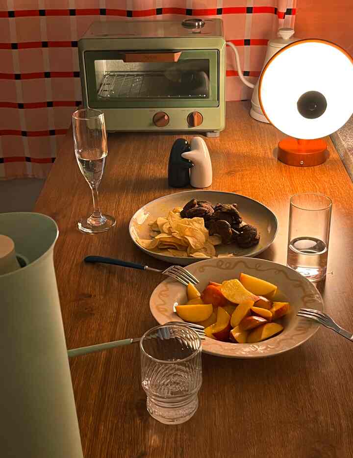 温かみのあるウッドトーンとオレンジ色の照明が印象的なホームカフェ風のダイニングスペース、レトロなオーブンとおやつが配置されている