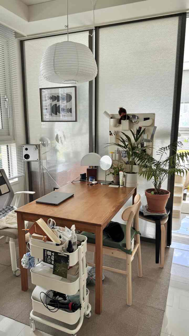 ベージュと木製のトーンの多目的ホームオフィス兼ダイニング空間、ペンダントライトと緑の植物が調和した室内