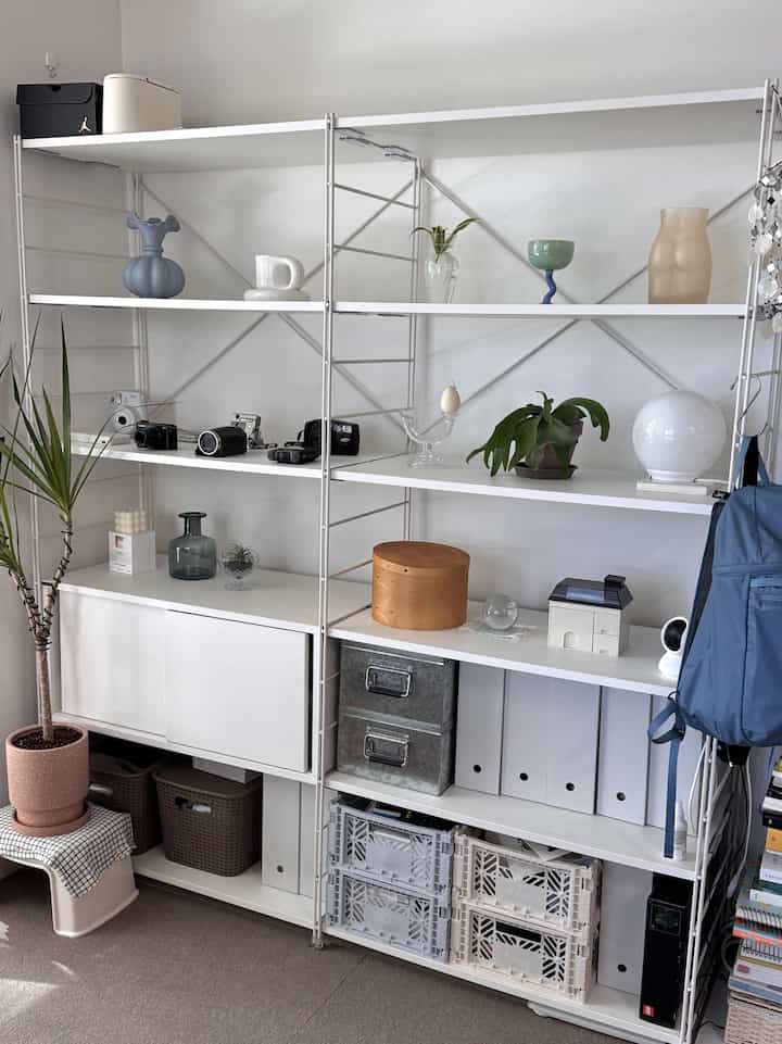 ホワイトとグレーの色調の空間、整理された棚と収納箱、オブジェが配置されたミニマルなインテリア