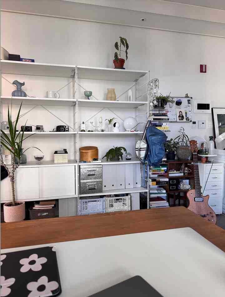 白い壁と棚が配されたモダンなホームオフィス空間、木製のテーブルとギターが温かみのある雰囲気を演出