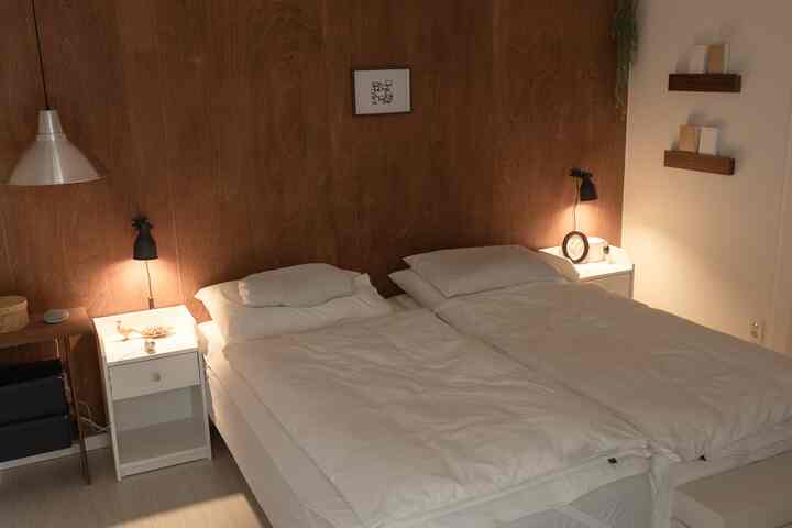 ナチュラルな木目調の壁と白いベッド、ナイトテーブル、ブラケットライトが配置された落ち着いた二人用寝室