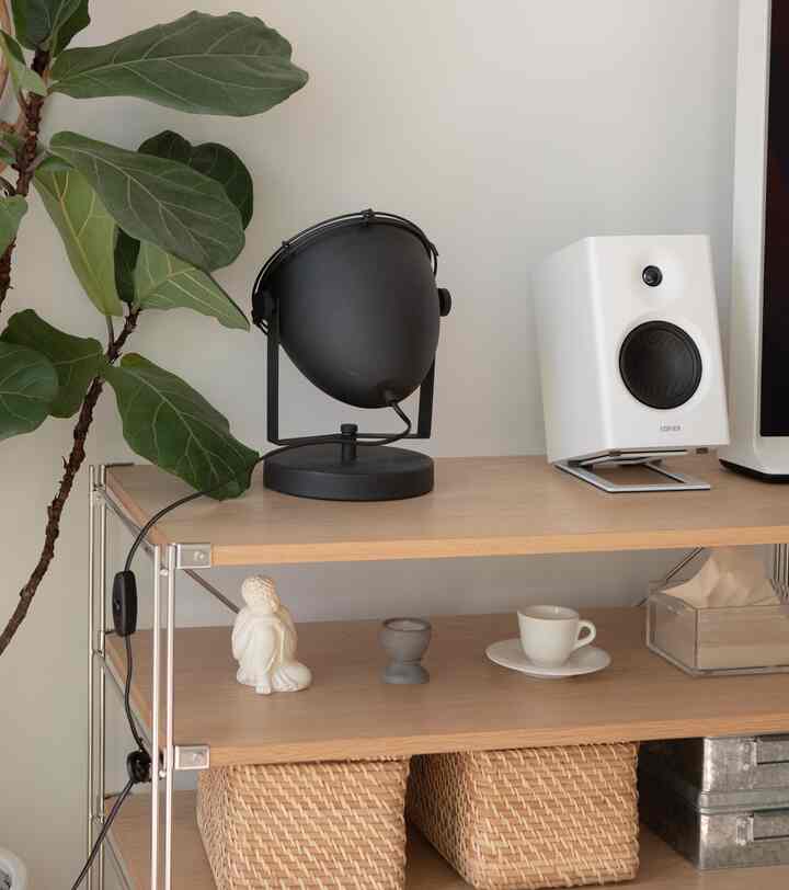 白い壁と木製の棚、黒いスタンドランプと白いスピーカーが配置されたシンプルでモダンな印象的な空間