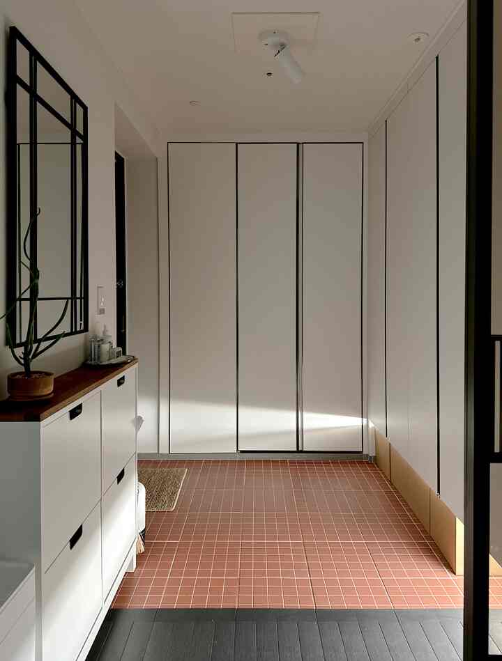 白と茶色の色調の玄関、広い靴棚と壁掛け鏡が配置された清潔でミニマルなインテリア