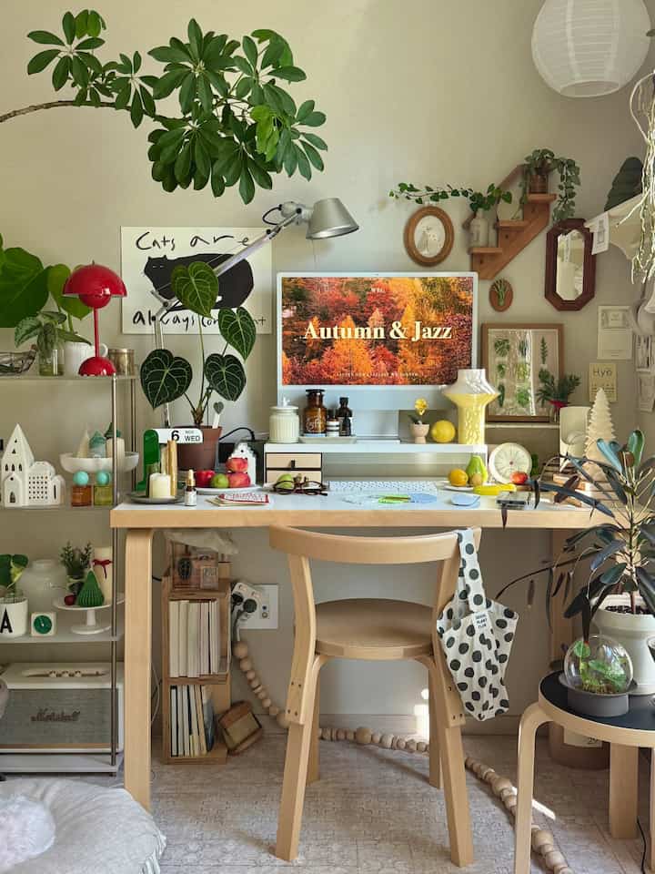 木目調のデスクと椅子が配置されたホームオフィス空間、様々な植物と額縁が壁に飾られ、温かみのある自然的な雰囲気を醸し出すインテリア