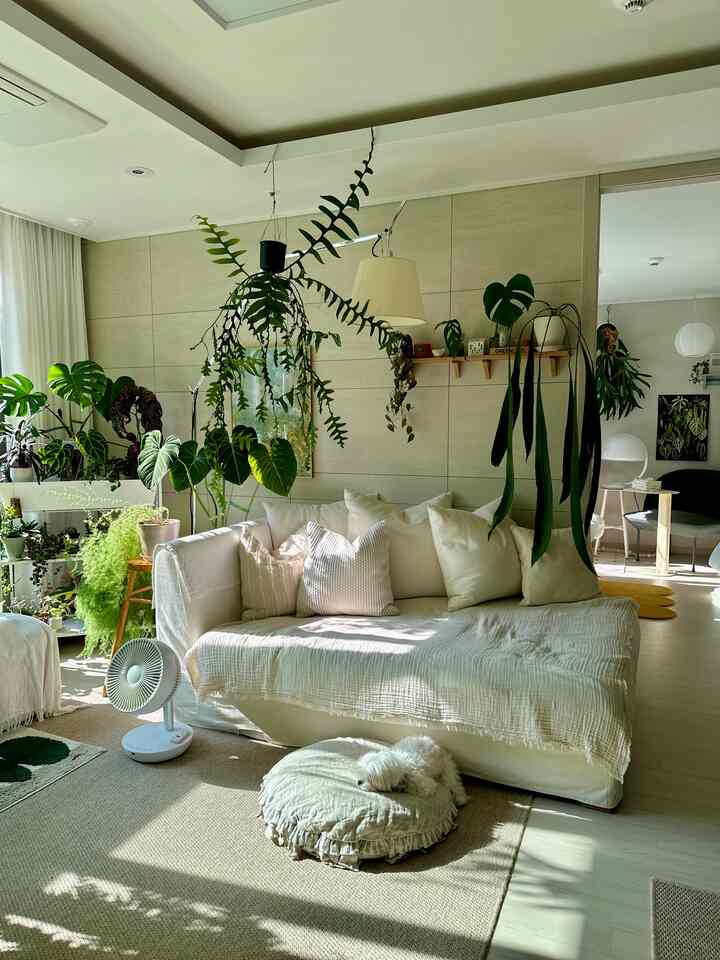 ナチュラルな色調のリビング、白いソファと豊富な緑の植物が配置された落ち着いた雰囲気の空間