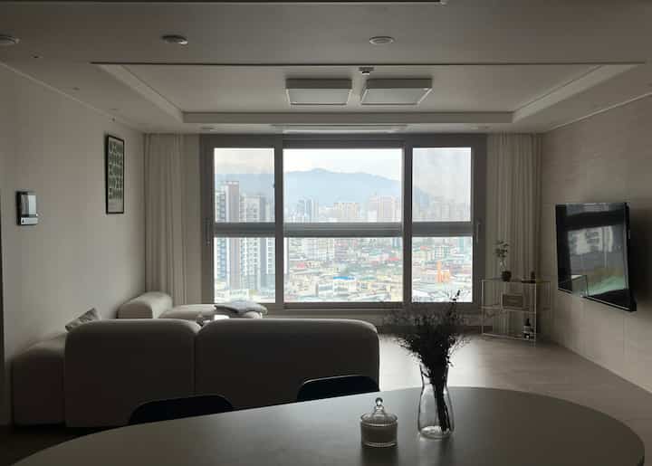 落ち着いたトーンのリビング、大きな窓と白いモジュラーソファが配置されたミニマルモダンな空間