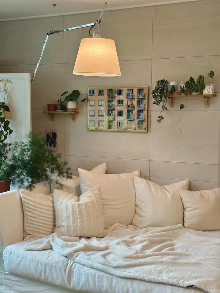 ベージュトーンのアートウォールとホワイトソファが配置された居心地の良いリビング、 大きなヘッドライトと植物が調和したインテリア