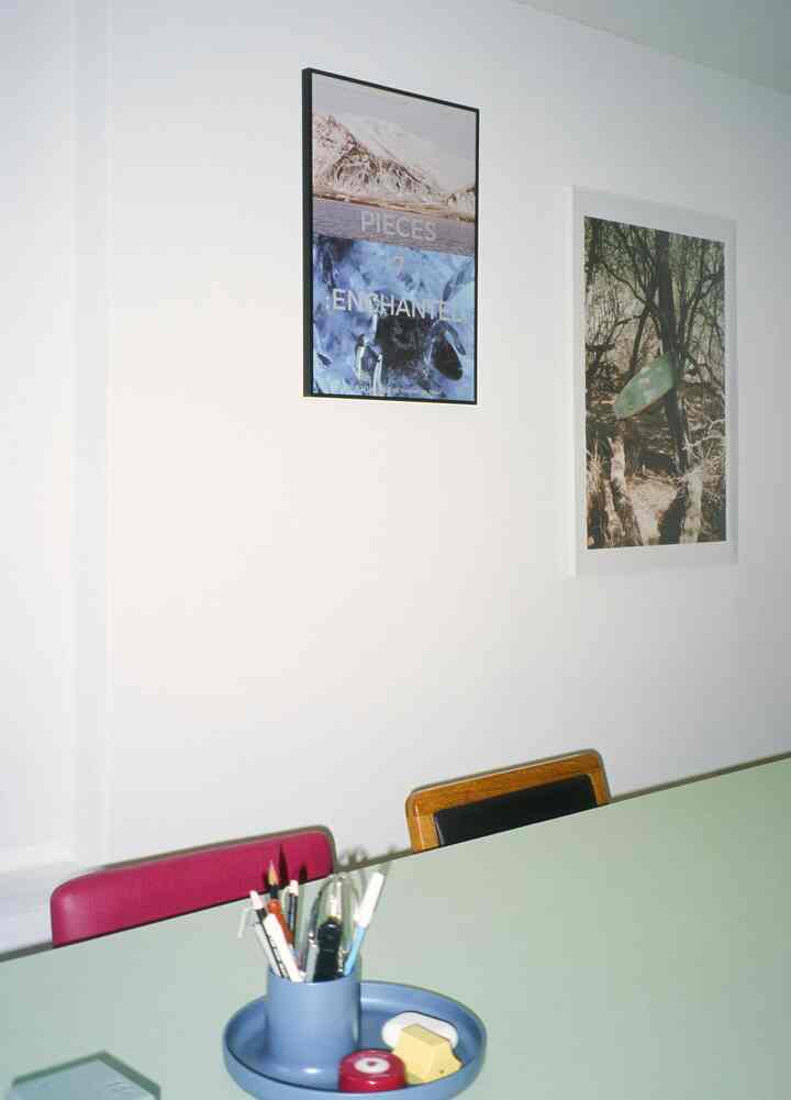 白い壁と緑のテーブルがあるダイニングルーム、壁にはアートが飾られ、テーブル上には文具が配置された雰囲気のある空間