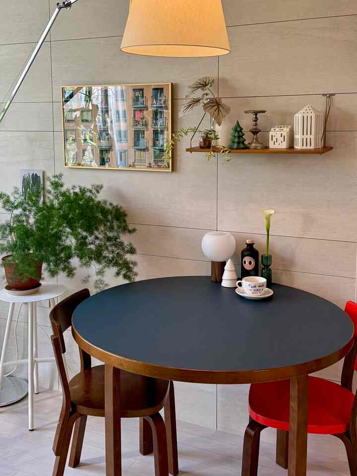 ナチュラルなベージュの壁とヴィンテージ風の丸いダイニングテーブル、椅子、植物、テーブルランプが配置されたダイニングルーム