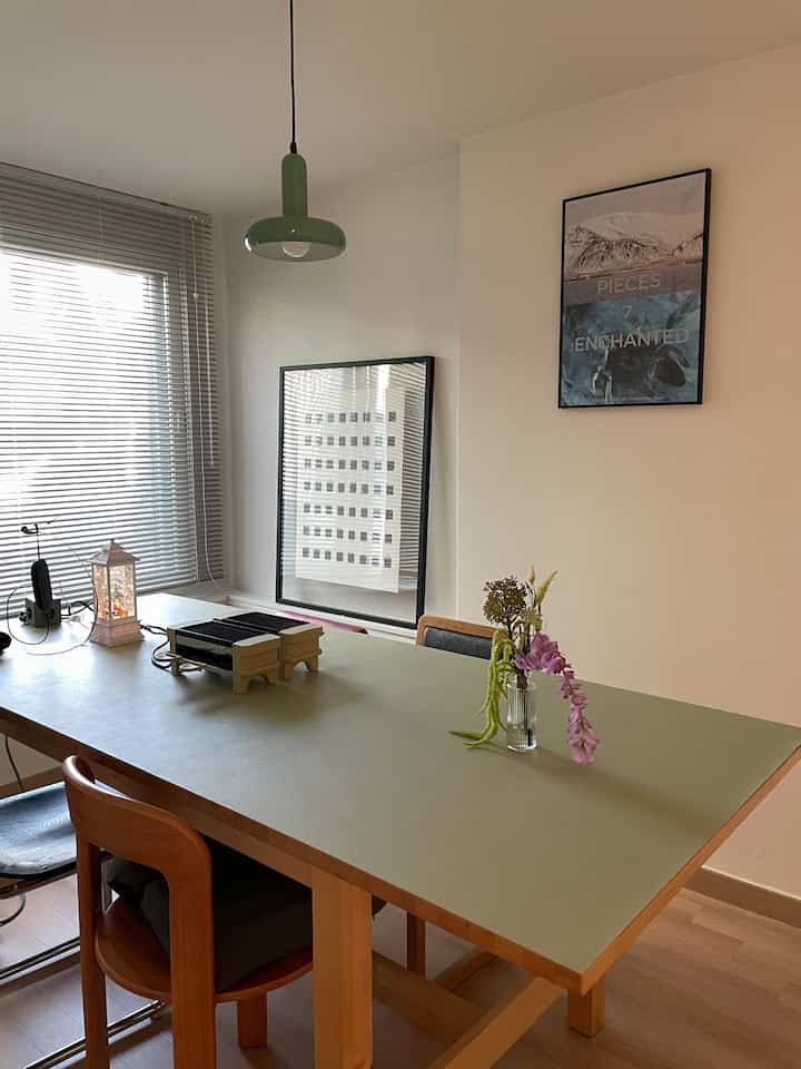 ナチュラルな木目調とライトグリーンのテーブルマットが目立つダイニング、ペンダントライトとインテリア写真が配置された雰囲気のある空間