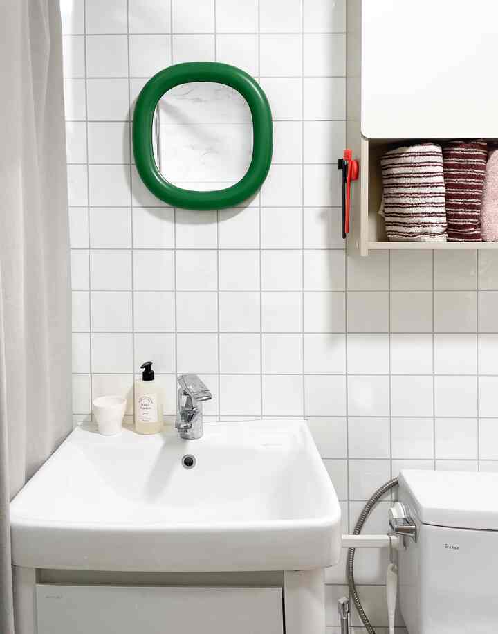 ホワイトタイルの壁と緑色のフレームミラーがある清潔なバスルーム、洗面台とタオルが配置された空間