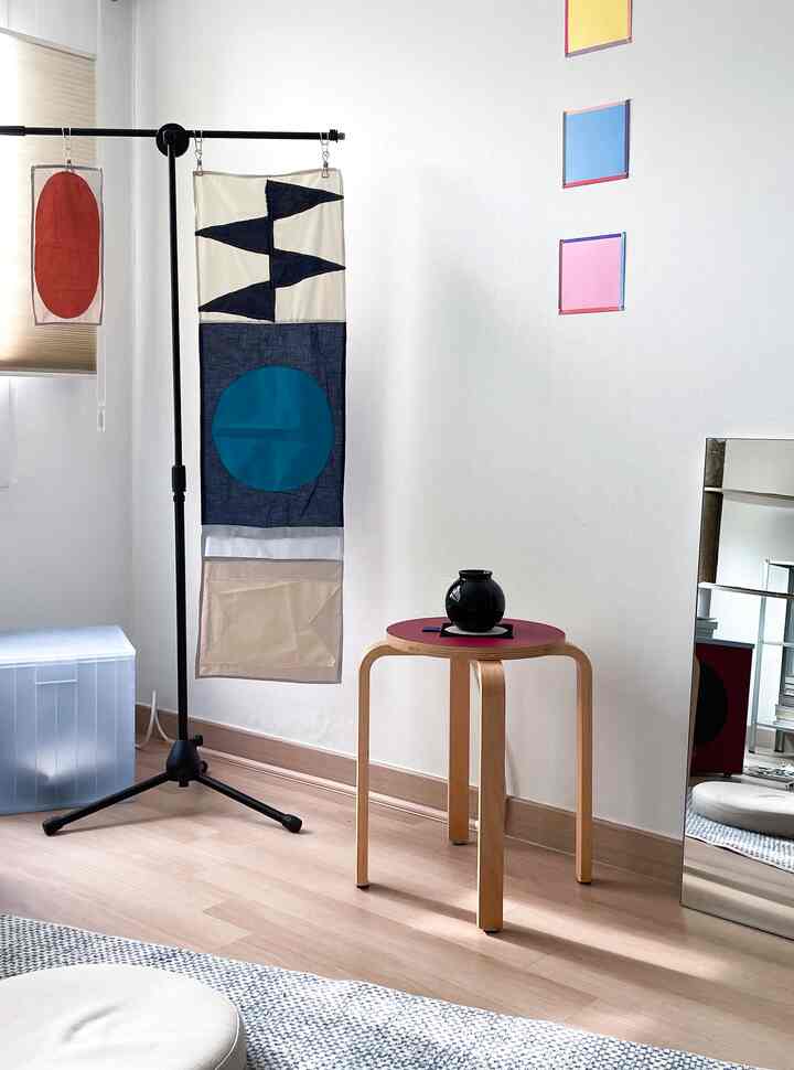 白い壁とナチュラルウッド調のスツールがあるミニマルな空間、スツールの上に黒いガラス製の花瓶とコースターが飾られている