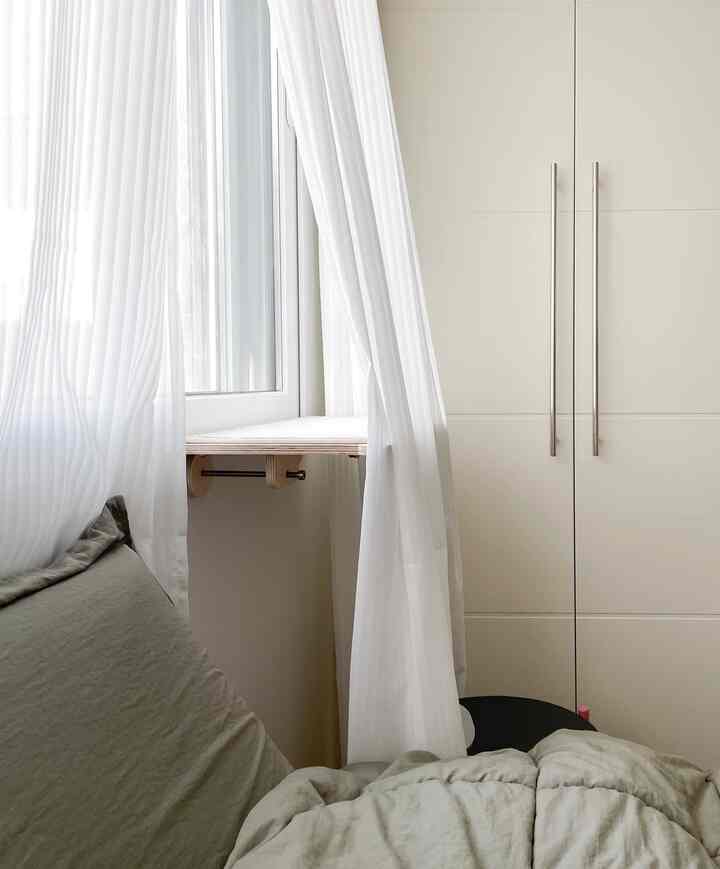 白いカーテンとベージュのクローゼットが配置されたナチュラルな寝室、猫用の窓棚が見える
