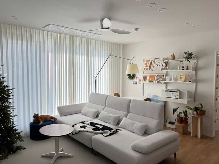 ホワイトとウッドトーンのリビング、広いソファとポスターや植物を配した棚が印象的なナチュラルな空間