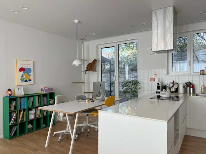 白と木目調の調和が美しいキッチンダイニング、キャットタワーの猫とホームオフィスのデスクが配置された清潔感のある空間