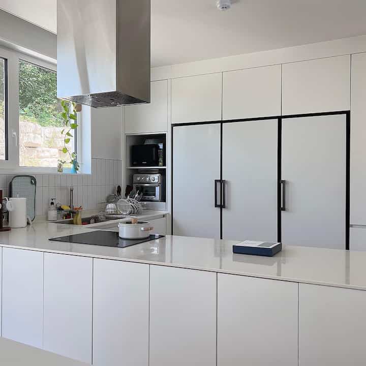 明るい白を基調としたモダンなキッチン、オブジェ冷蔵庫とビルトイン家電が整然と配置された洗練された空間