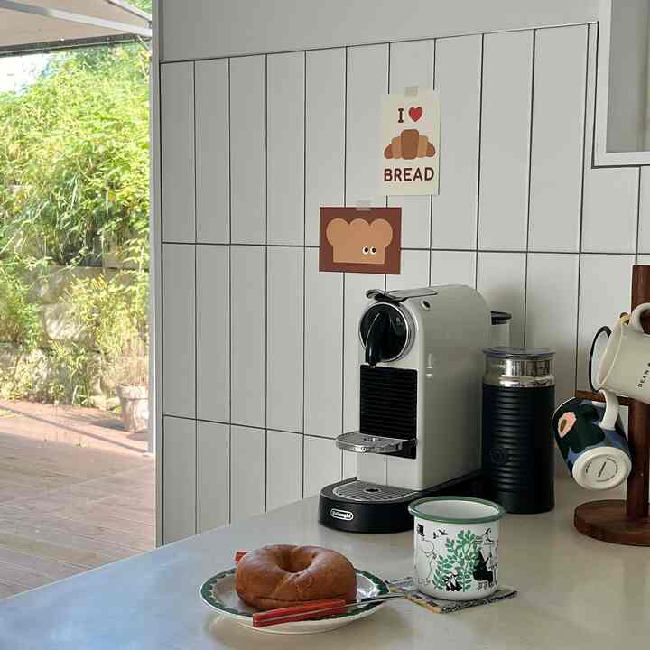 白いタイル壁とモダンなキッチンカウンターにコーヒーマシンとマグカップが置かれた清潔感のあるおうちカフェ空間