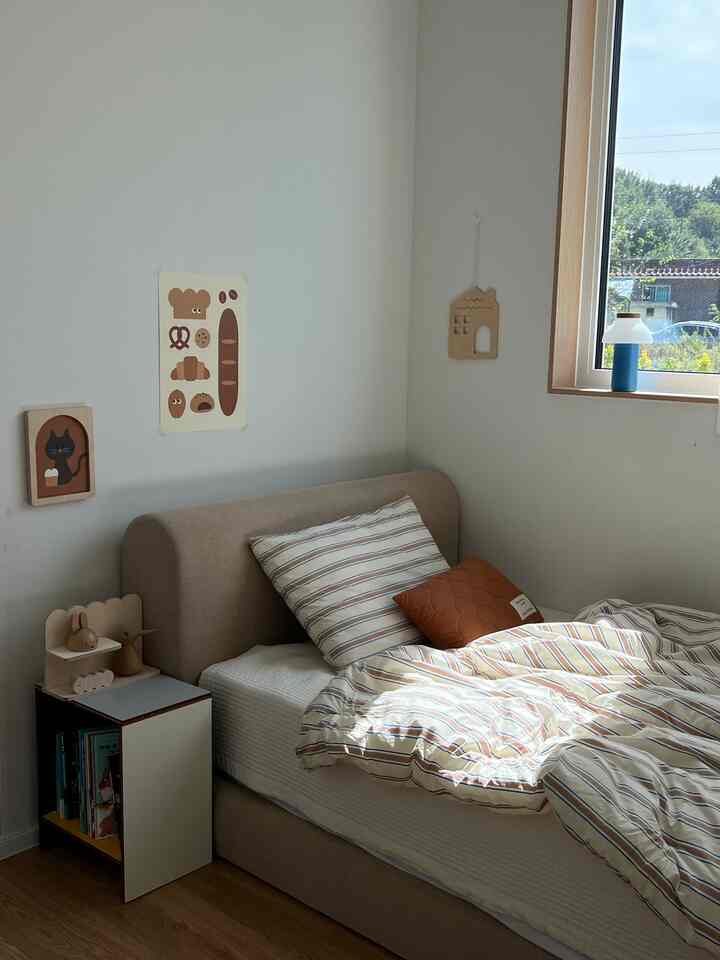 ナチュラルで木目調の子供部屋、ベージュのベッドと白い壁、窓から自然光が差し込む温かみのあるインテリア