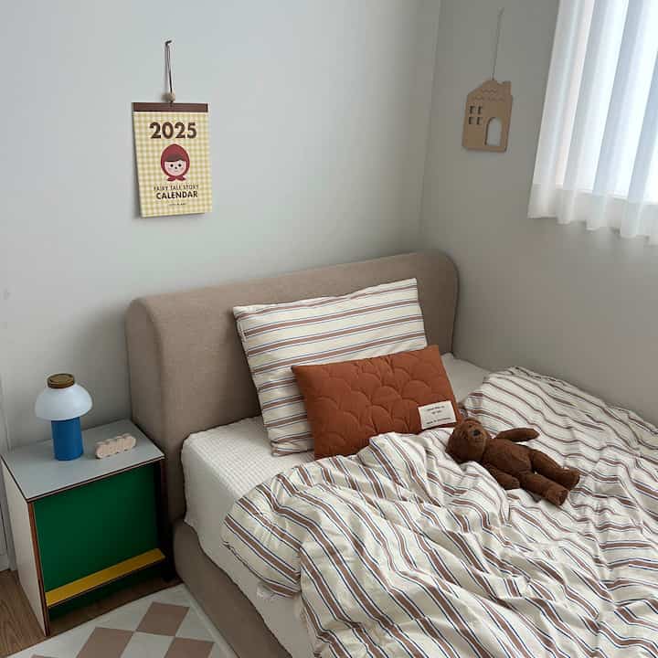 ナチュラルカラーの子供部屋で、ベージュのベッドとストライプの寝具、木製のインテリアが配置された温かみのある空間