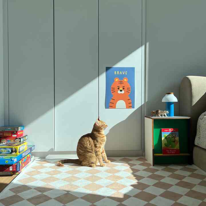 白とベージュの色調の子供部屋、猫とポスター、ナイトテーブル、ラグが配置された雰囲気のあるインテリア