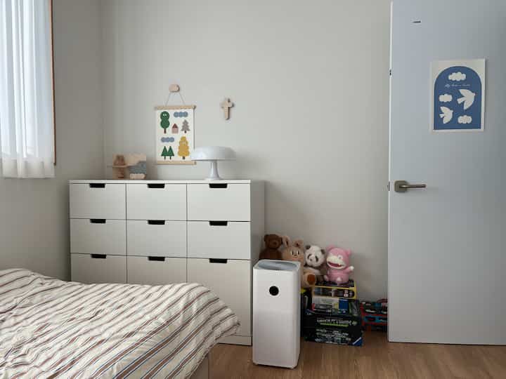 白と木目調の調和が取れた子供部屋、大きなチェストとおもちゃ、空気清浄機が配置された清潔で実用的なインテリア