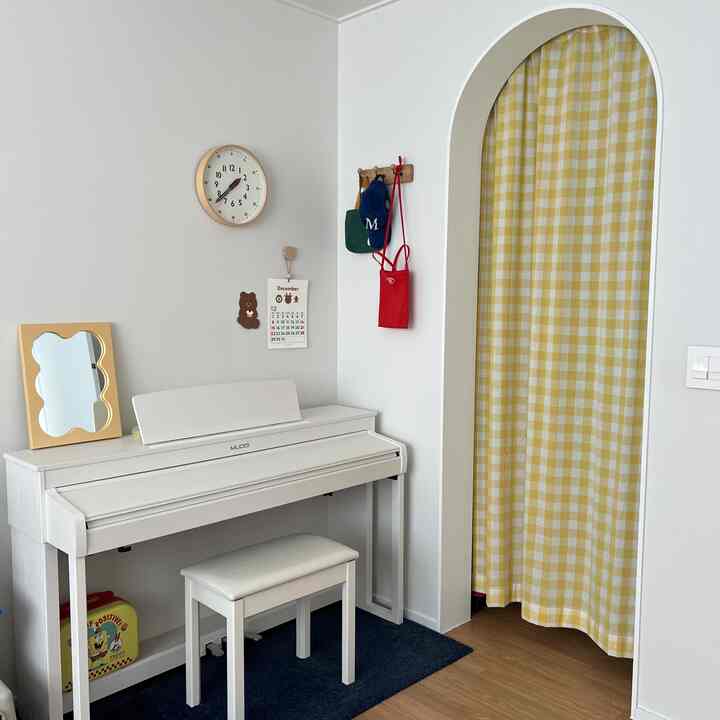 白と黄色の調和が取れた子供部屋、電子ピアノと格子模様の間仕切りカーテンが配置された雰囲気のある空間